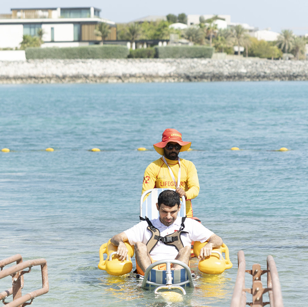 Lifeguard assisting a person in a floating beach wheelchair in shallow sea water