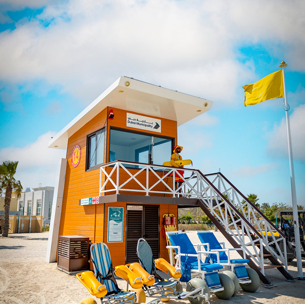 Orange lifeguard tower with a yellow flag and beach wheelchairs parked beside it